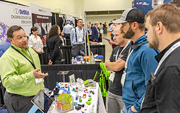 Attendees speak with exhibitor about his plastic components