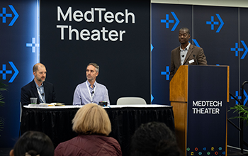 Moderator speaks as two panelists listen on the MedTech Theater stage