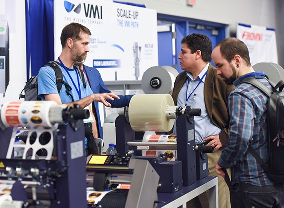 Attendees inspect various packaging products at an exhibit booth